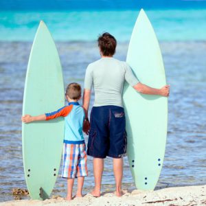 Back view of father and son with surfboards at beach